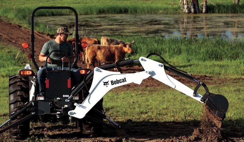 A man is using a bobcat tractor backhoe in a field.