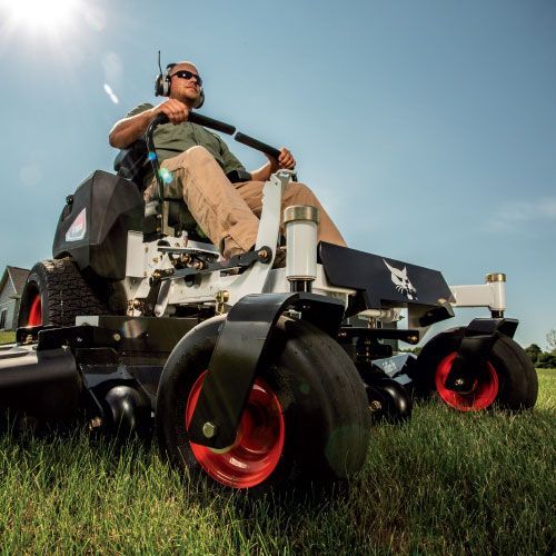 A man is riding a bobcat  mower in a grassy field.