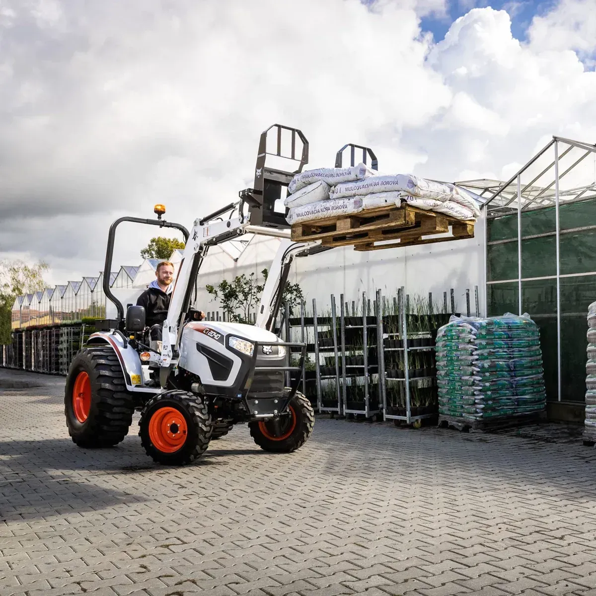 A man is driving a bobcat tractor with a forklift attached to it.