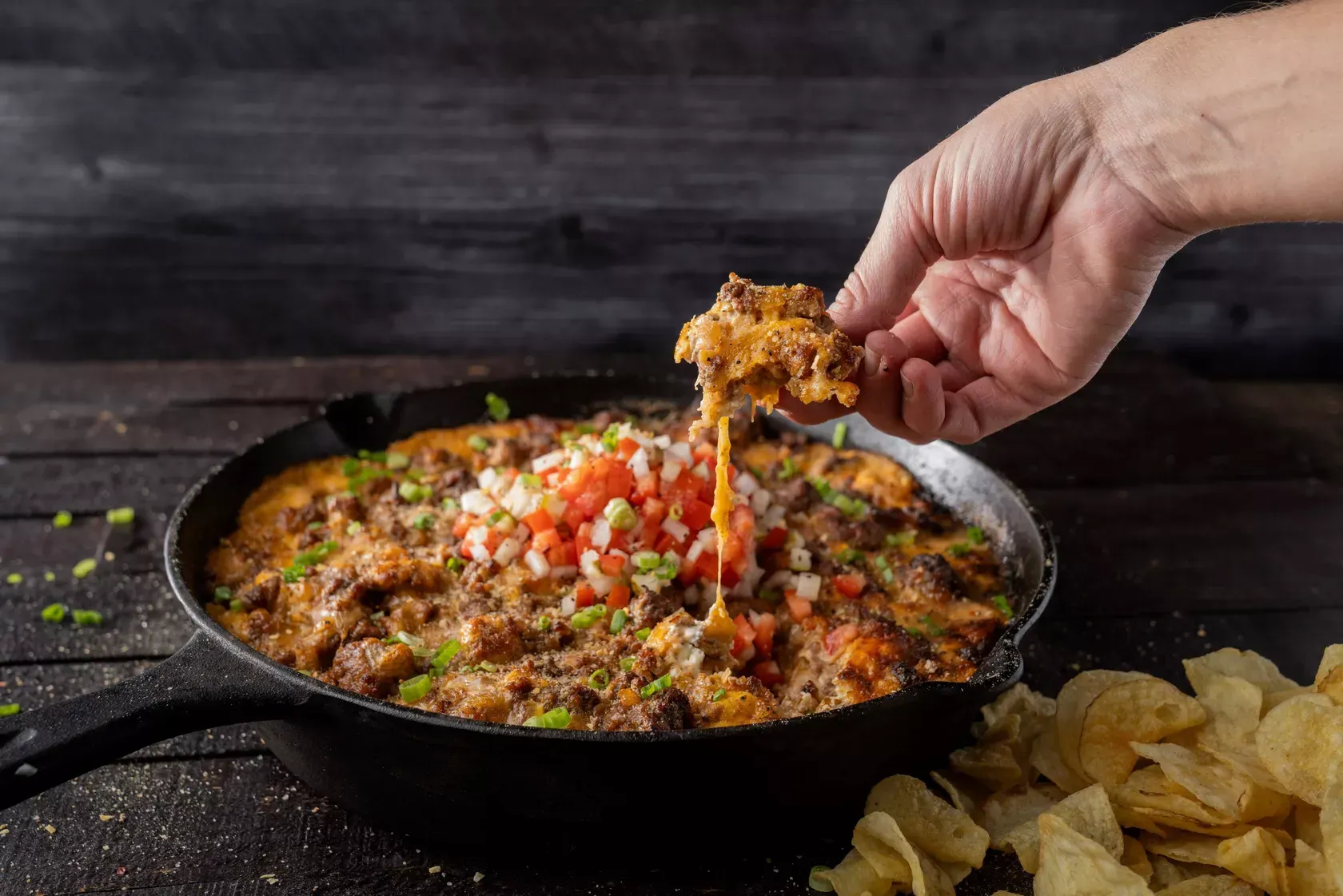 A person is dipping a chip into a skillet of food.