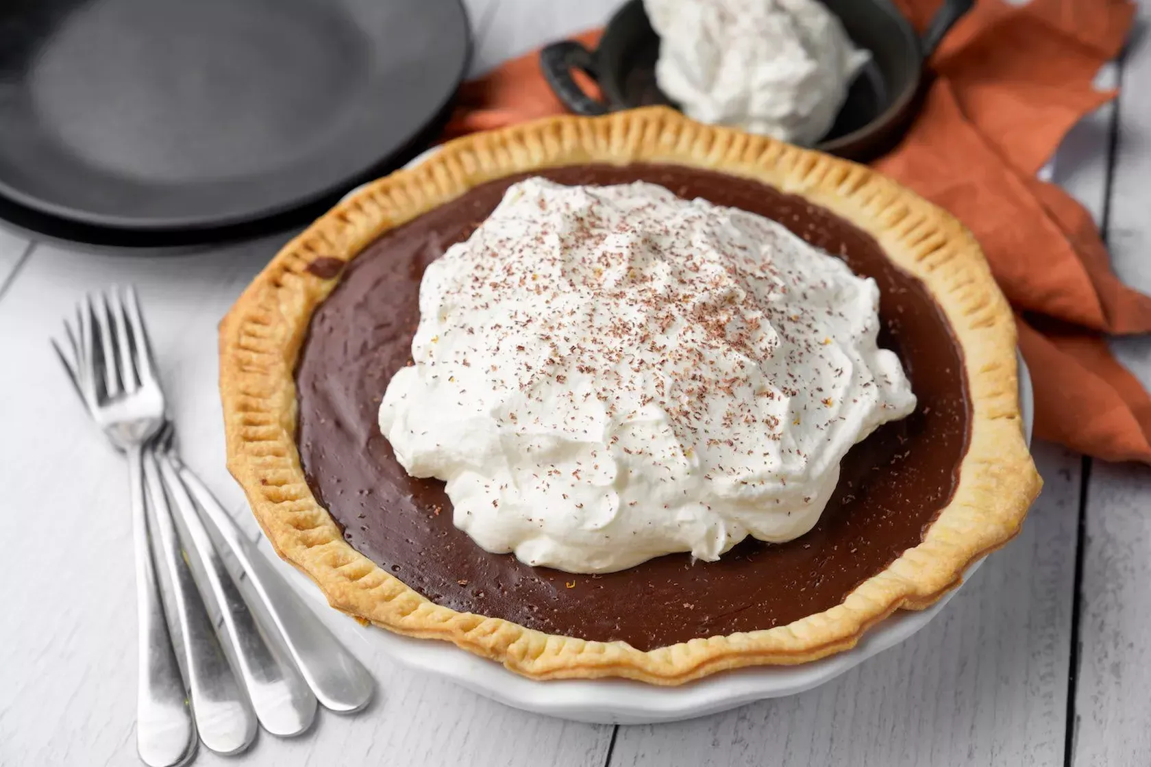 A chocolate pie with whipped cream on top is on a plate on a table.