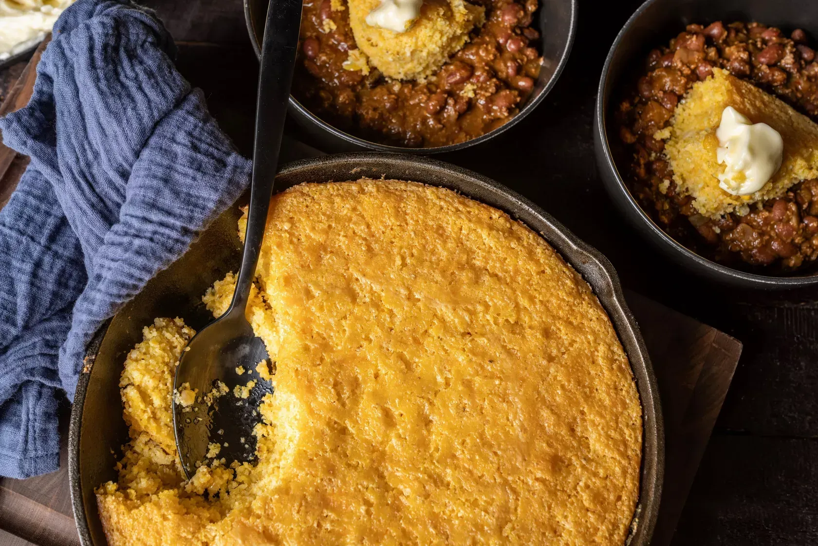 A skillet filled with cornbread and beans with a spoon in it.