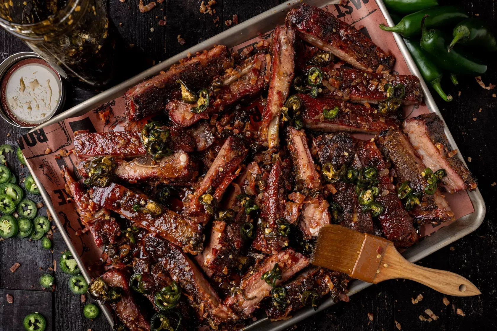 A tray of ribs with a wooden brush on a table.