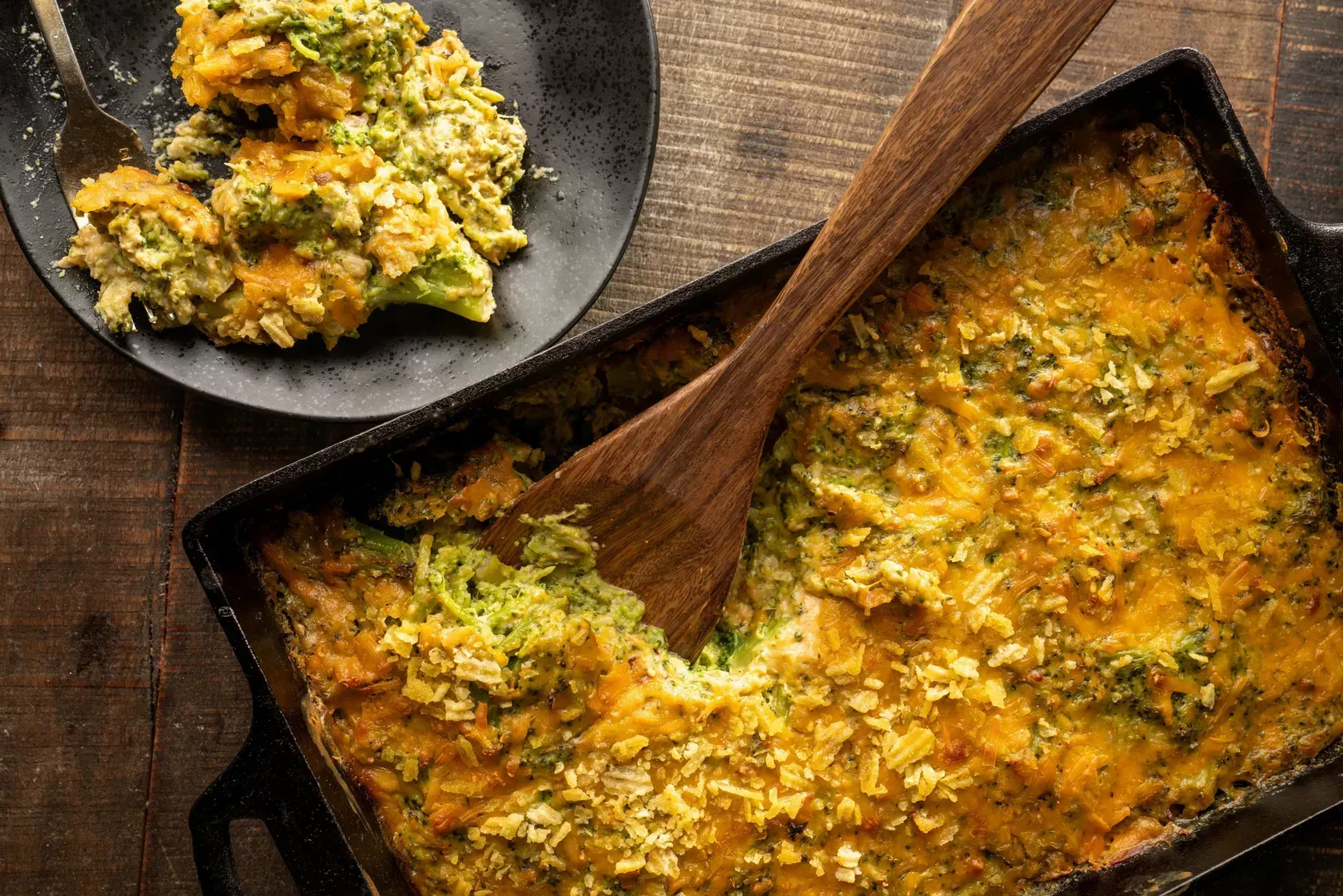 A casserole dish with a wooden spoon in it and a plate of food next to it.