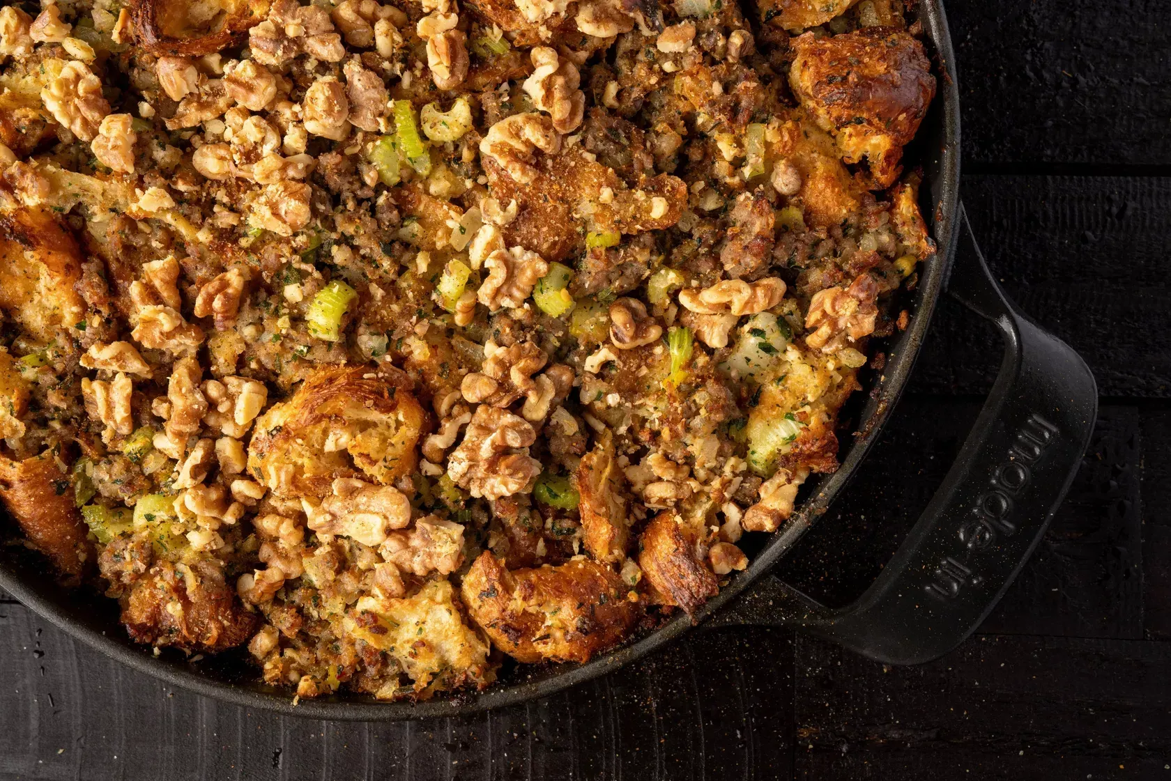 Close-up of baked stuffing with walnuts and celery in a cast iron dish.