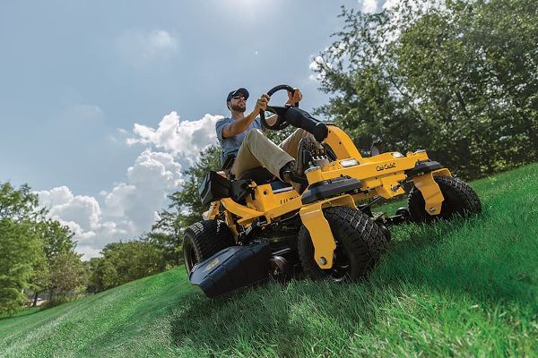 A man is riding a yellow lawn mower on a hill.