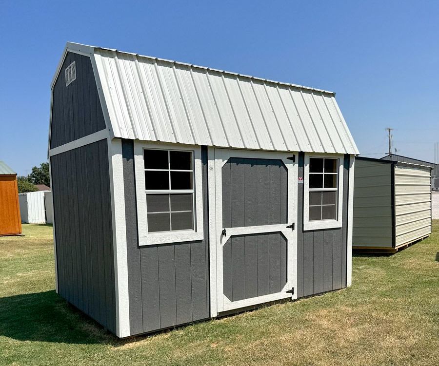 A gray and white barn shed is sitting in the middle of a grassy field.