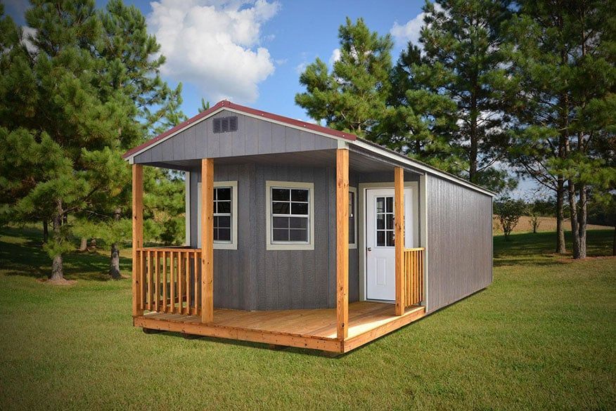 A Derksen portable cabin with a porch and trees in the background.