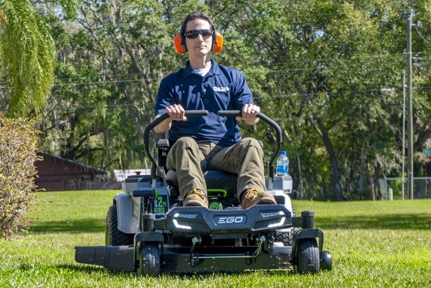 A man is riding a zero turn lawn mower on a lush green field.