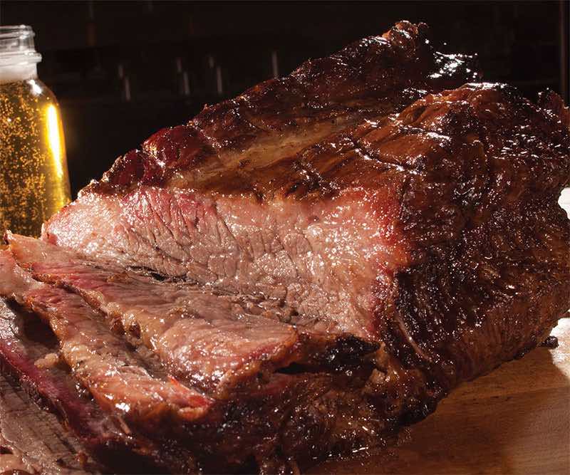 A large piece of meat is sitting on a cutting board next to a glass of beer