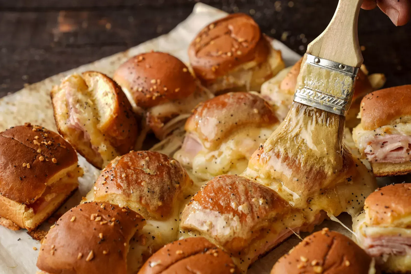 Baked sliders being brushed with a buttery glaze.