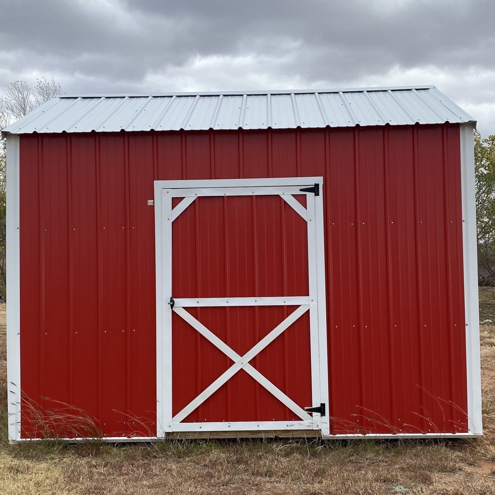A red side utility barn with a white door and a cloudy sky in the background
