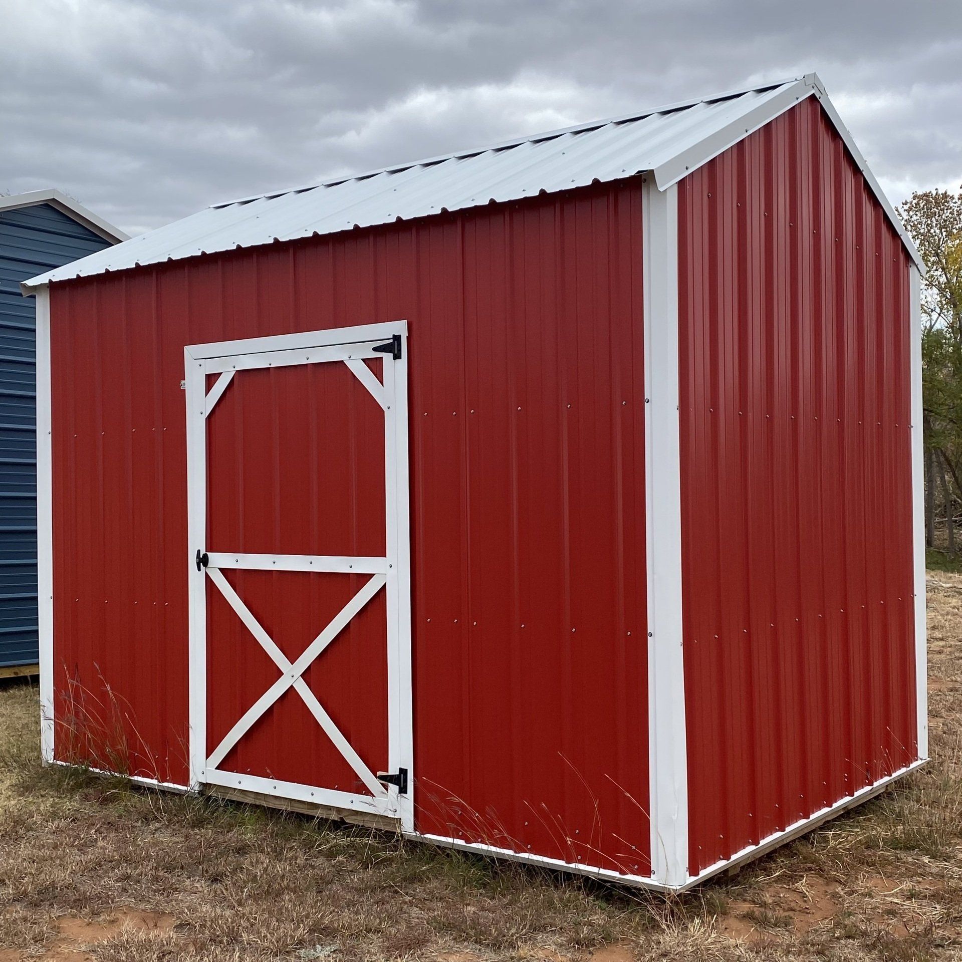 A red side utility barn with a white door is sitting in a field.
