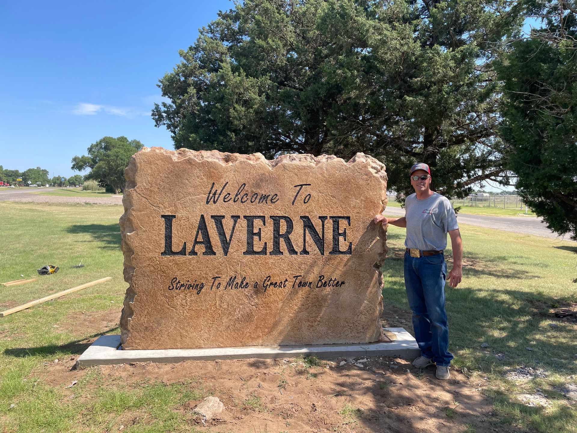 A man is standing in front of a large stone sign that says welcome to laverne.