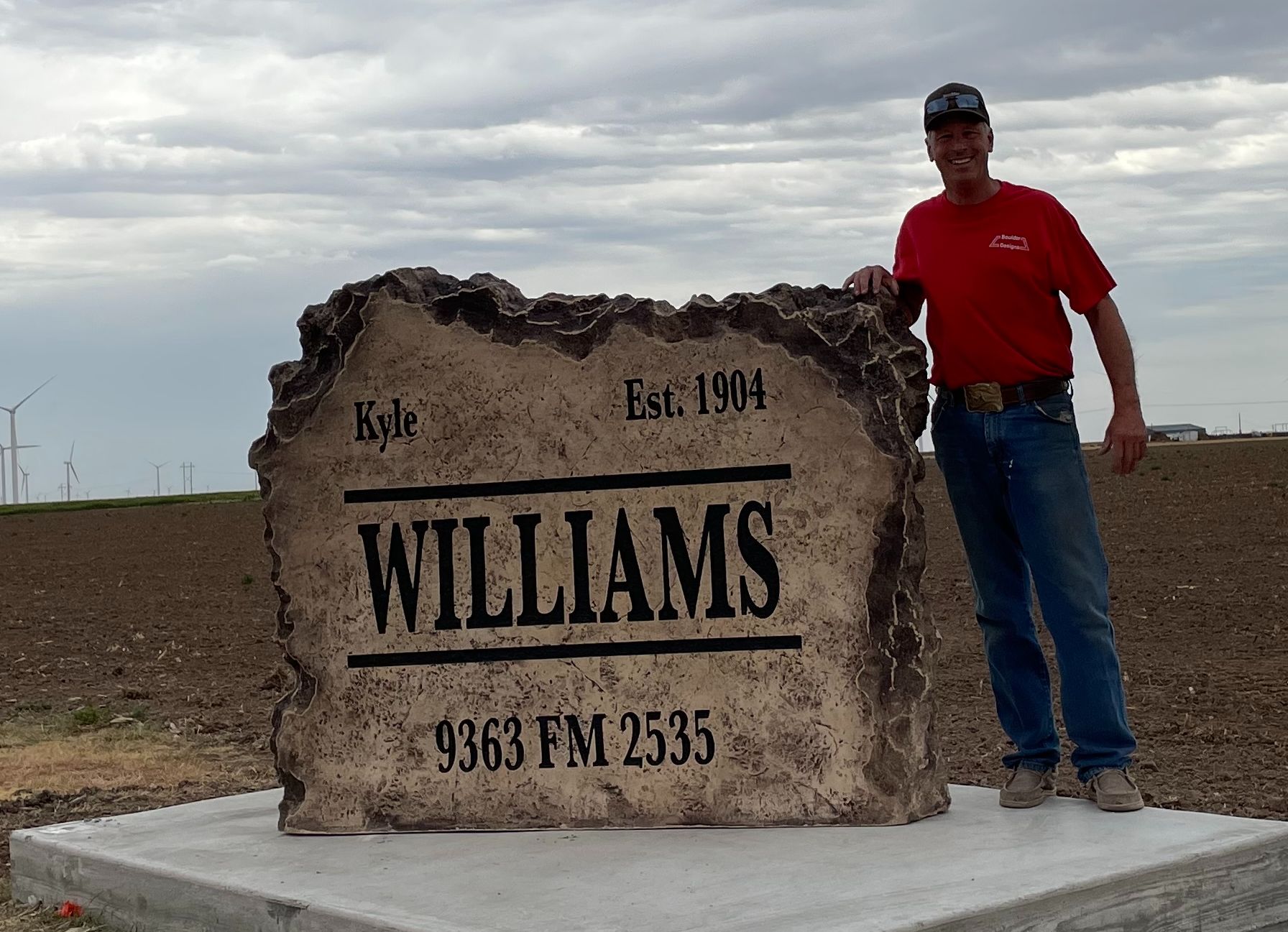 A man in a red shirt stands in front of a williams sign
