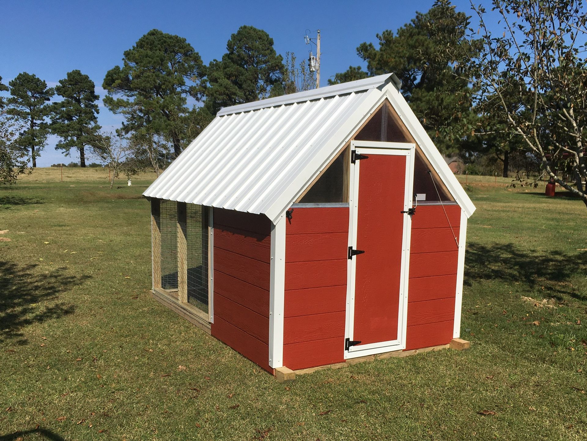 a red and white chicken coop is sitting in the middle of a grassy field .