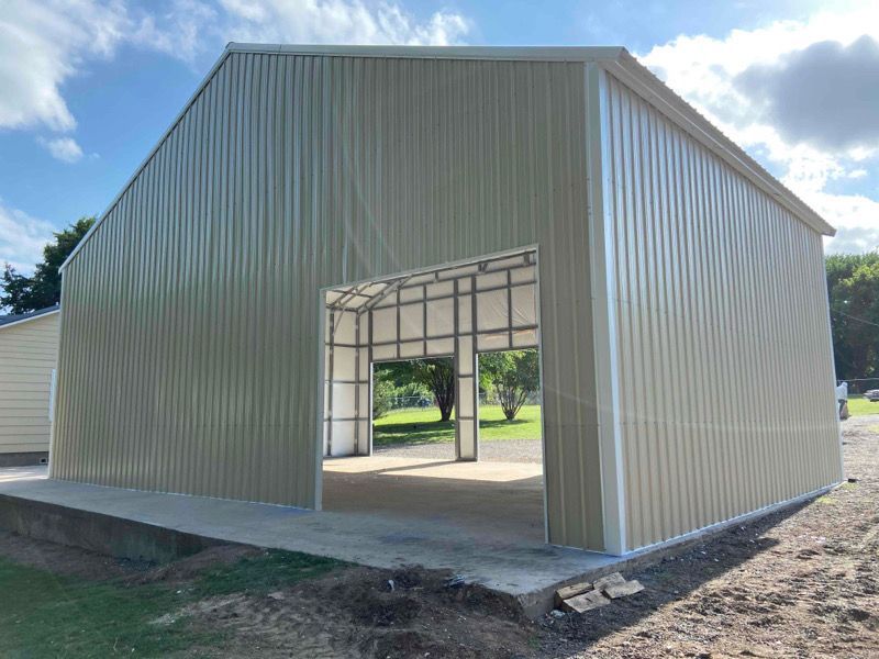 A large metal building with a large garage door is sitting on top of a dirt field.