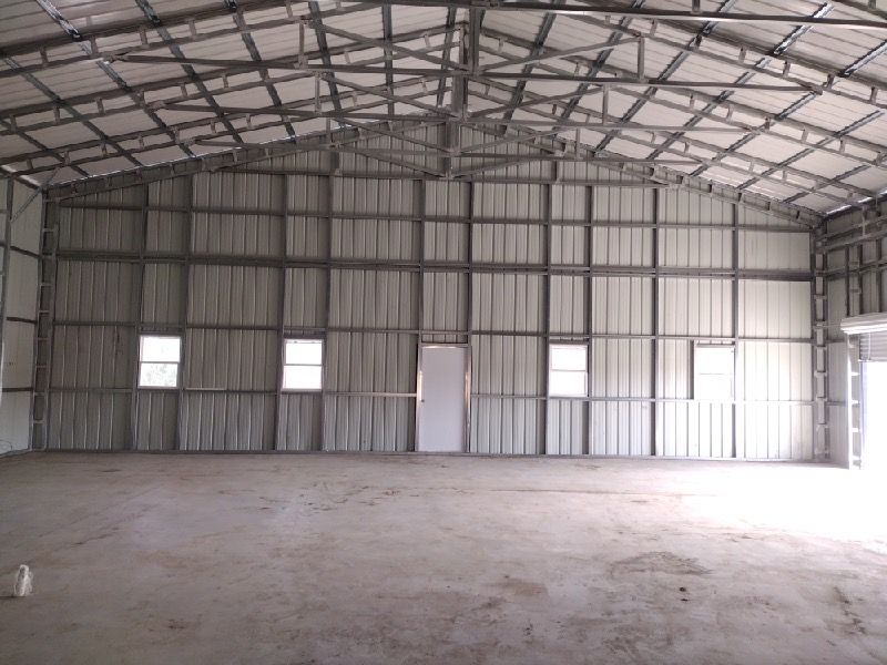 A large empty warehouse with a metal roof and a lot of windows.