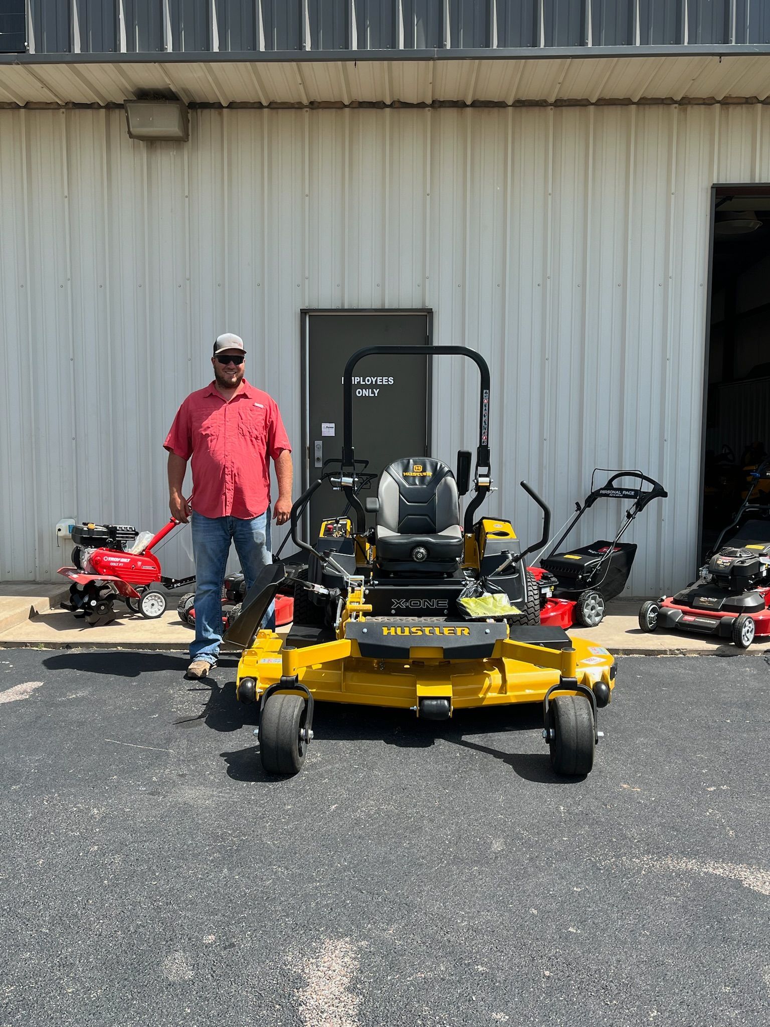 A man is standing next to a yellow lawn mower in front of a building.