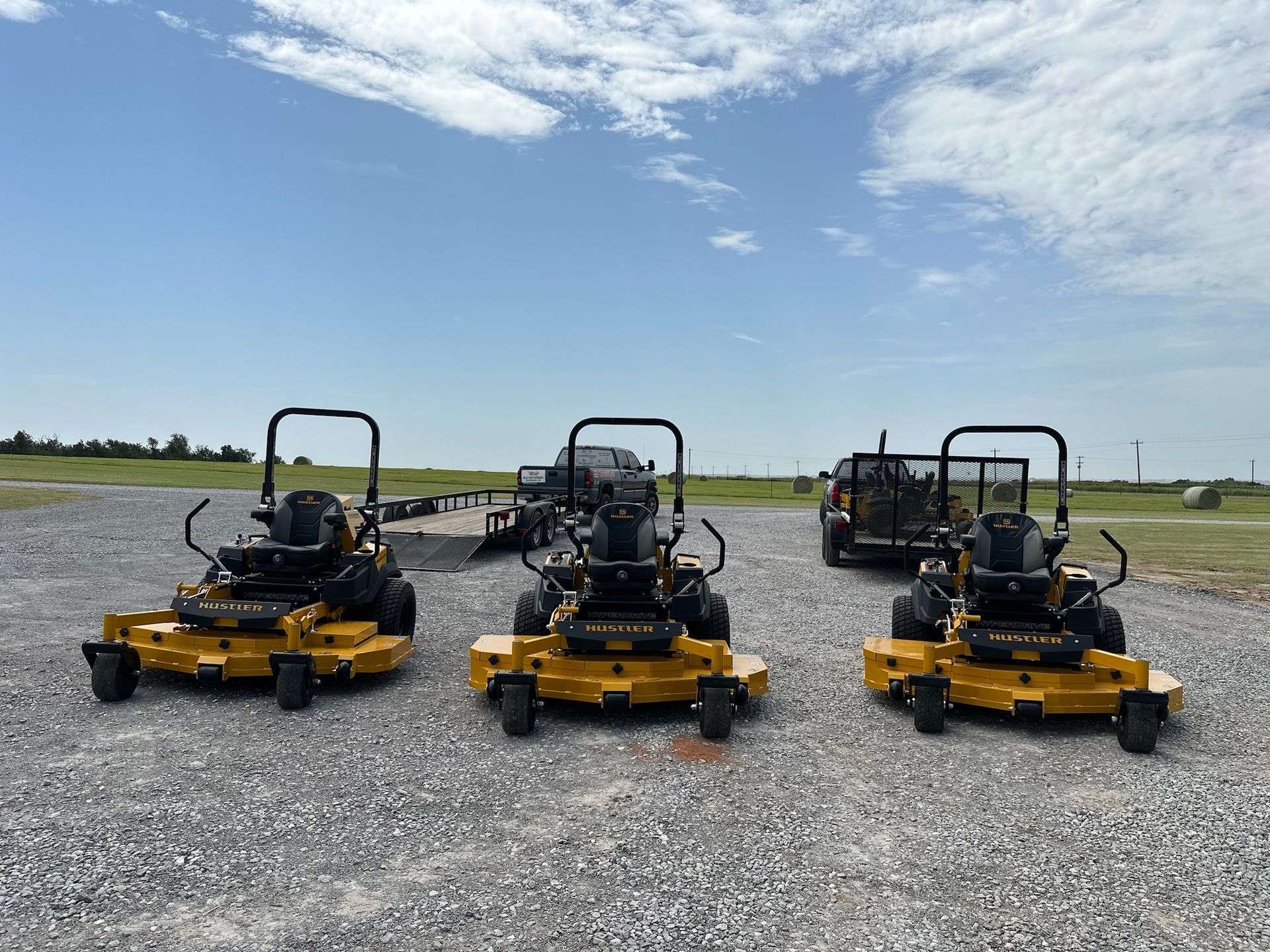 three yellow lawn mowers are parked in a gravel lot .