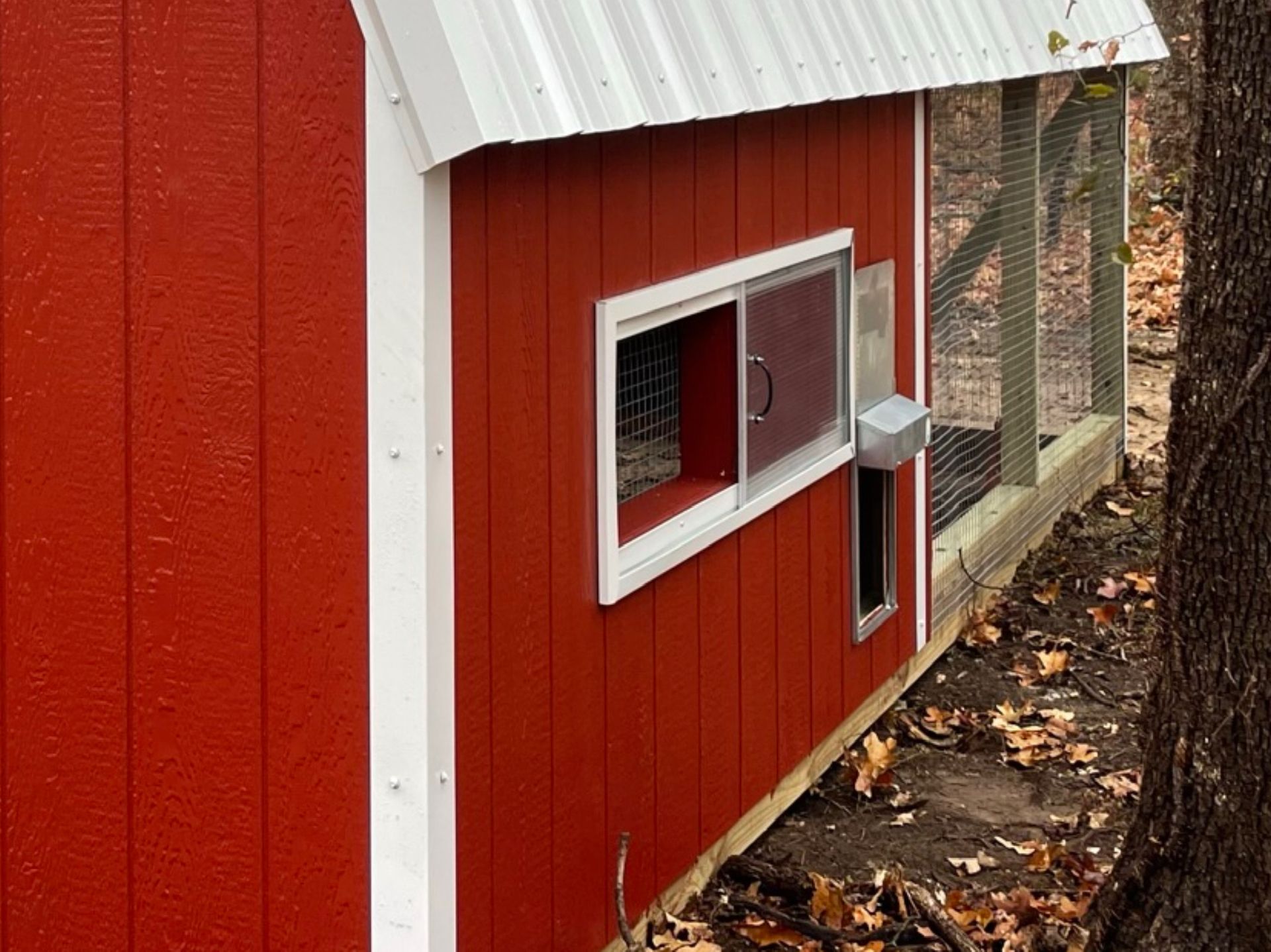 a red chicken coop with a white roof and a window