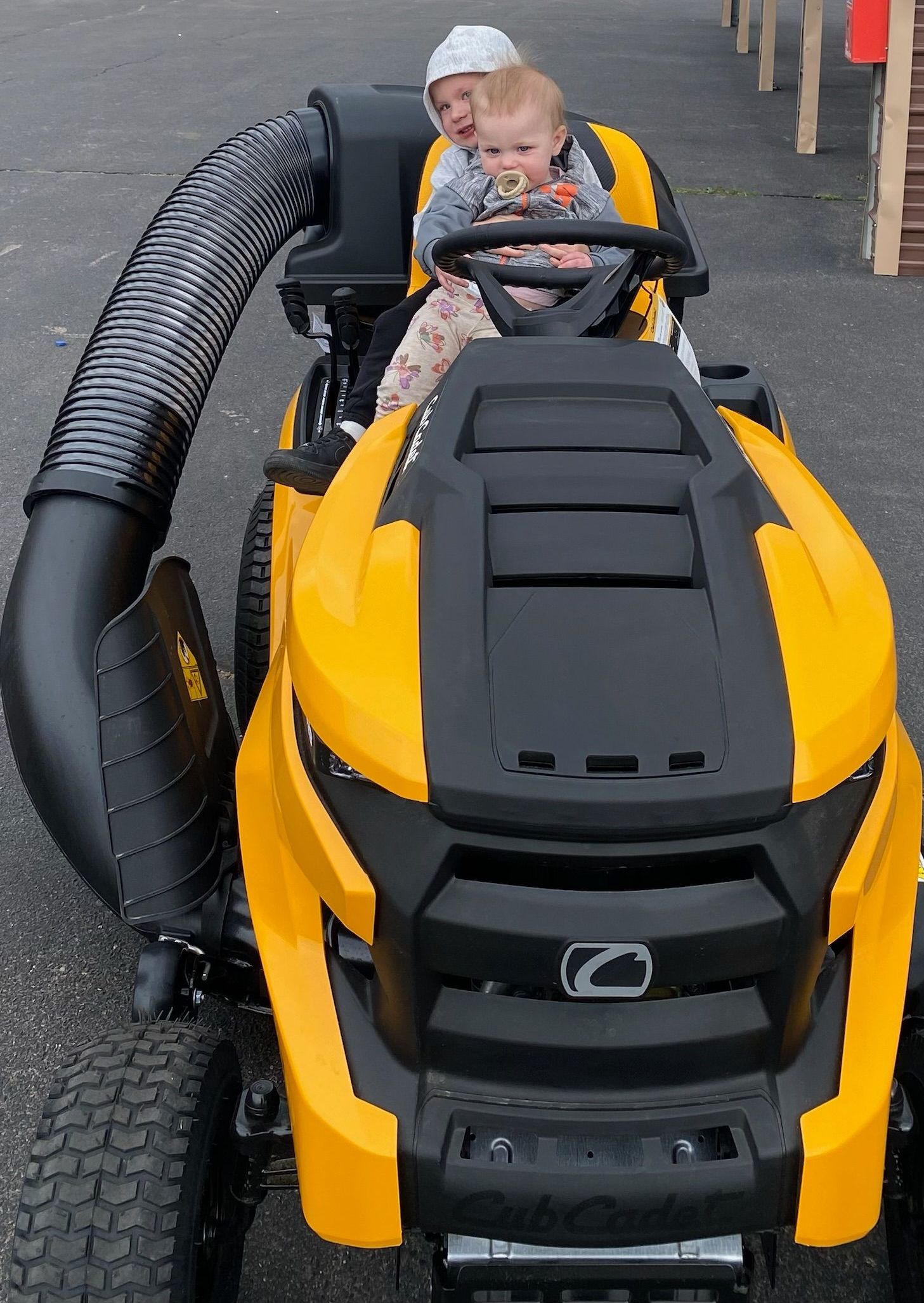 Two children are riding on a yellow and black lawn mower.