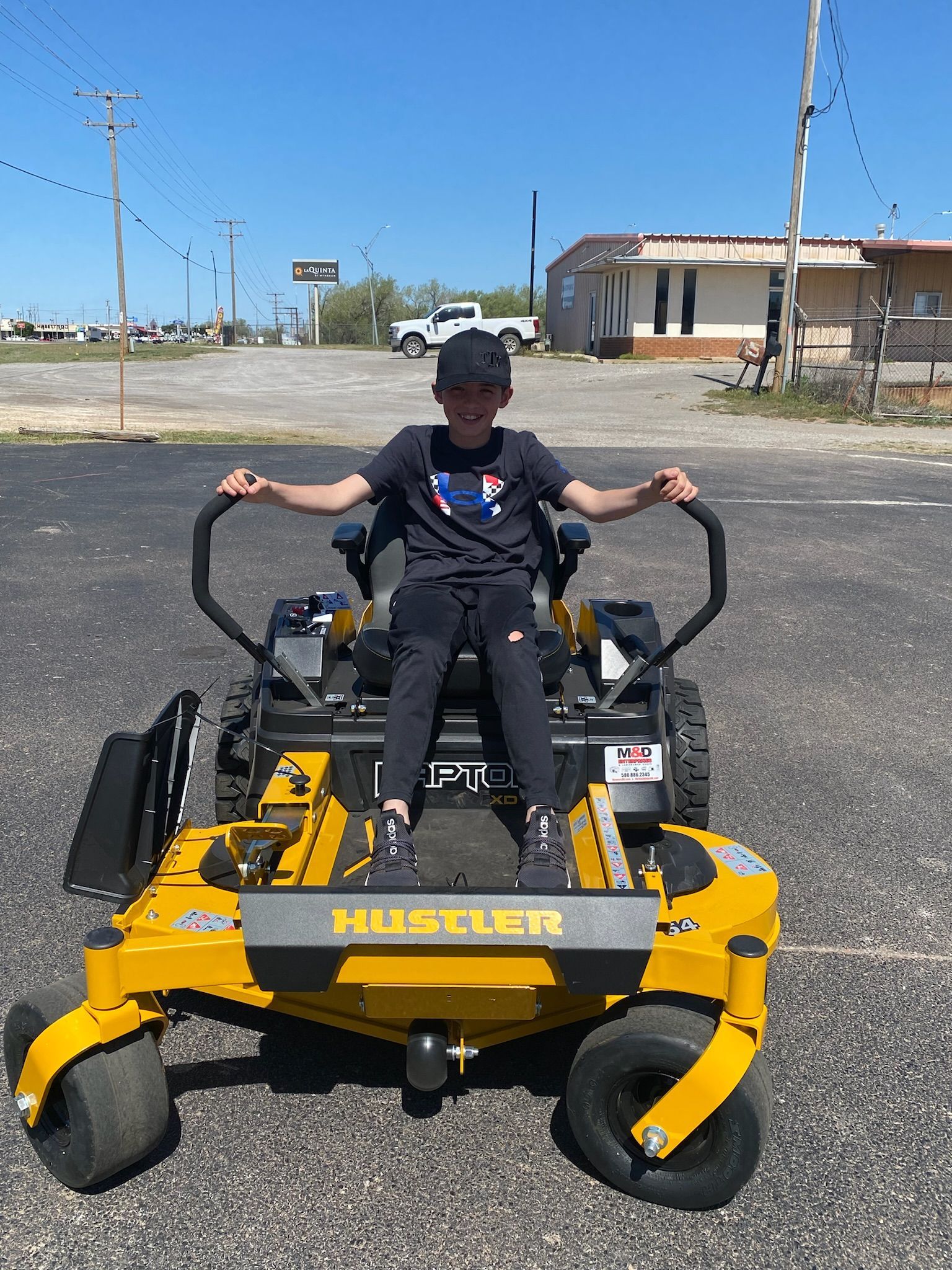 A young boy is sitting on a yellow lawn mower in a parking lot.