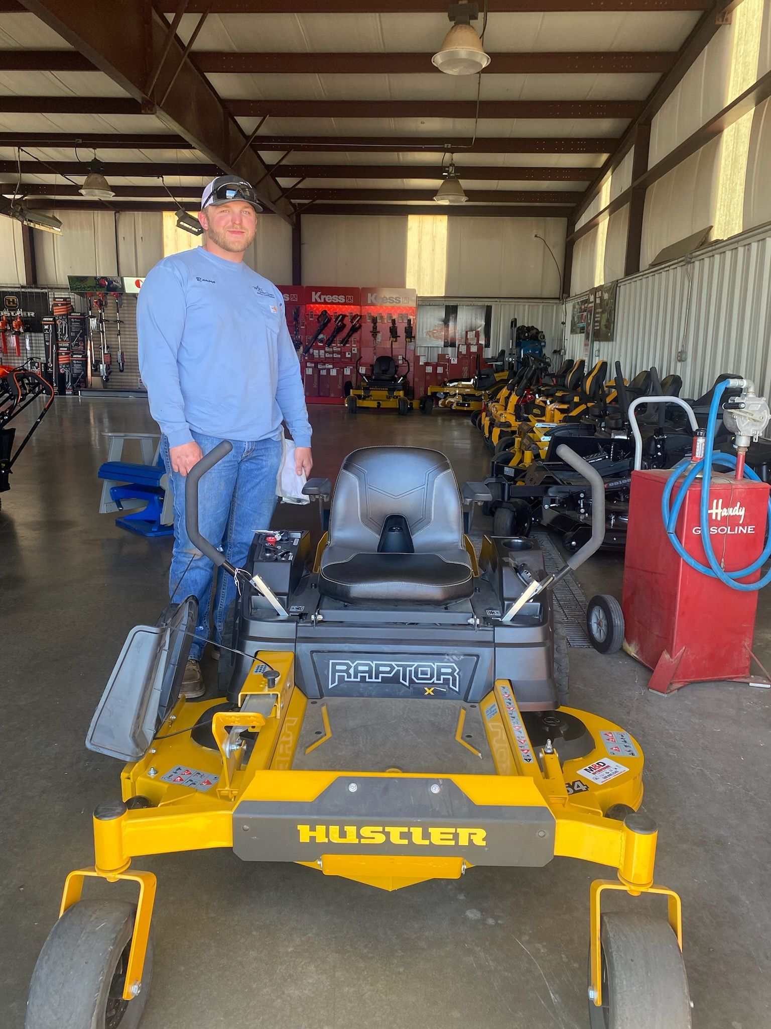 A man is standing next to a yellow and gray lawn mower in a warehouse.