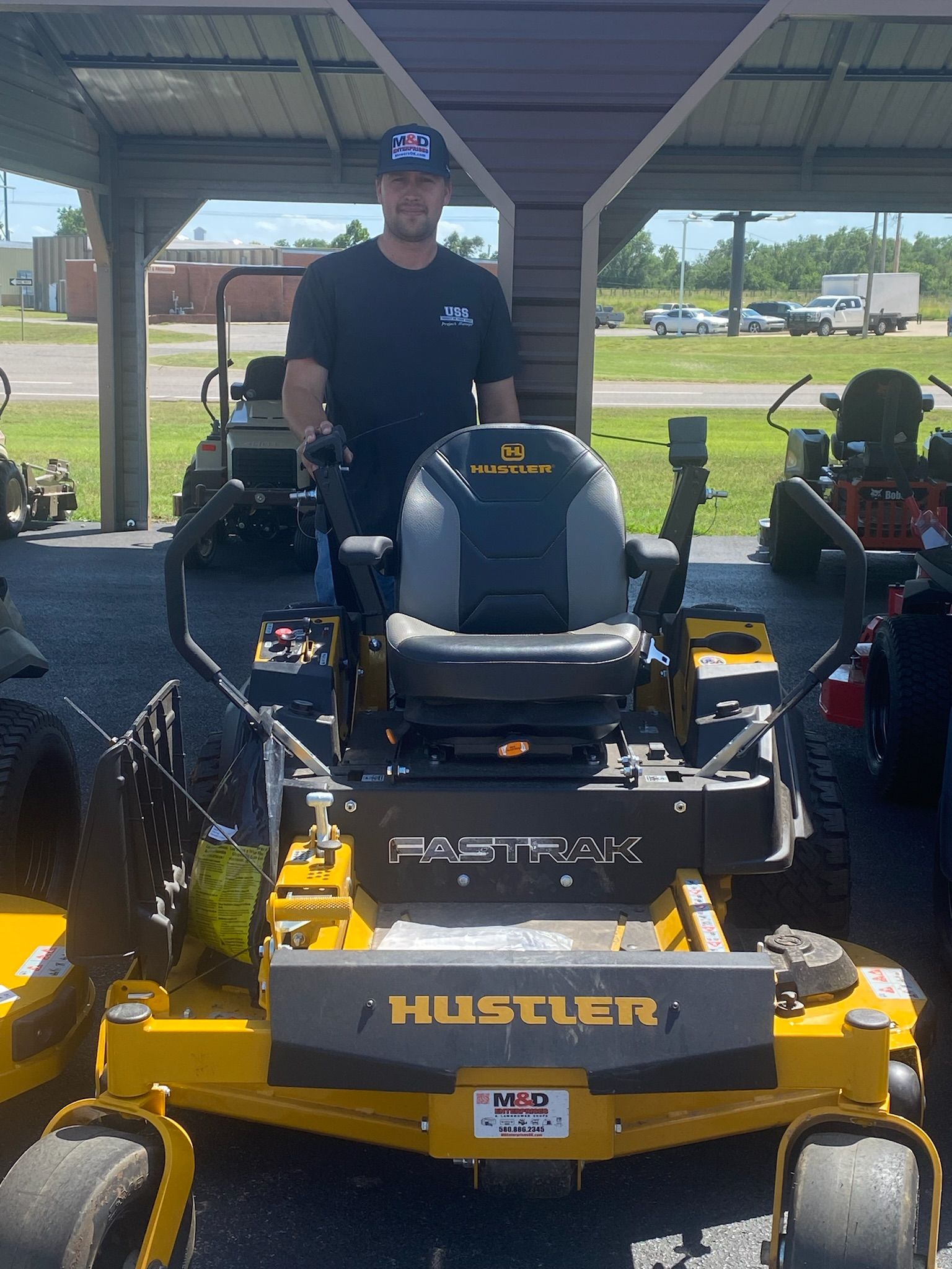 A man is standing next to a yellow hustler lawn mower.