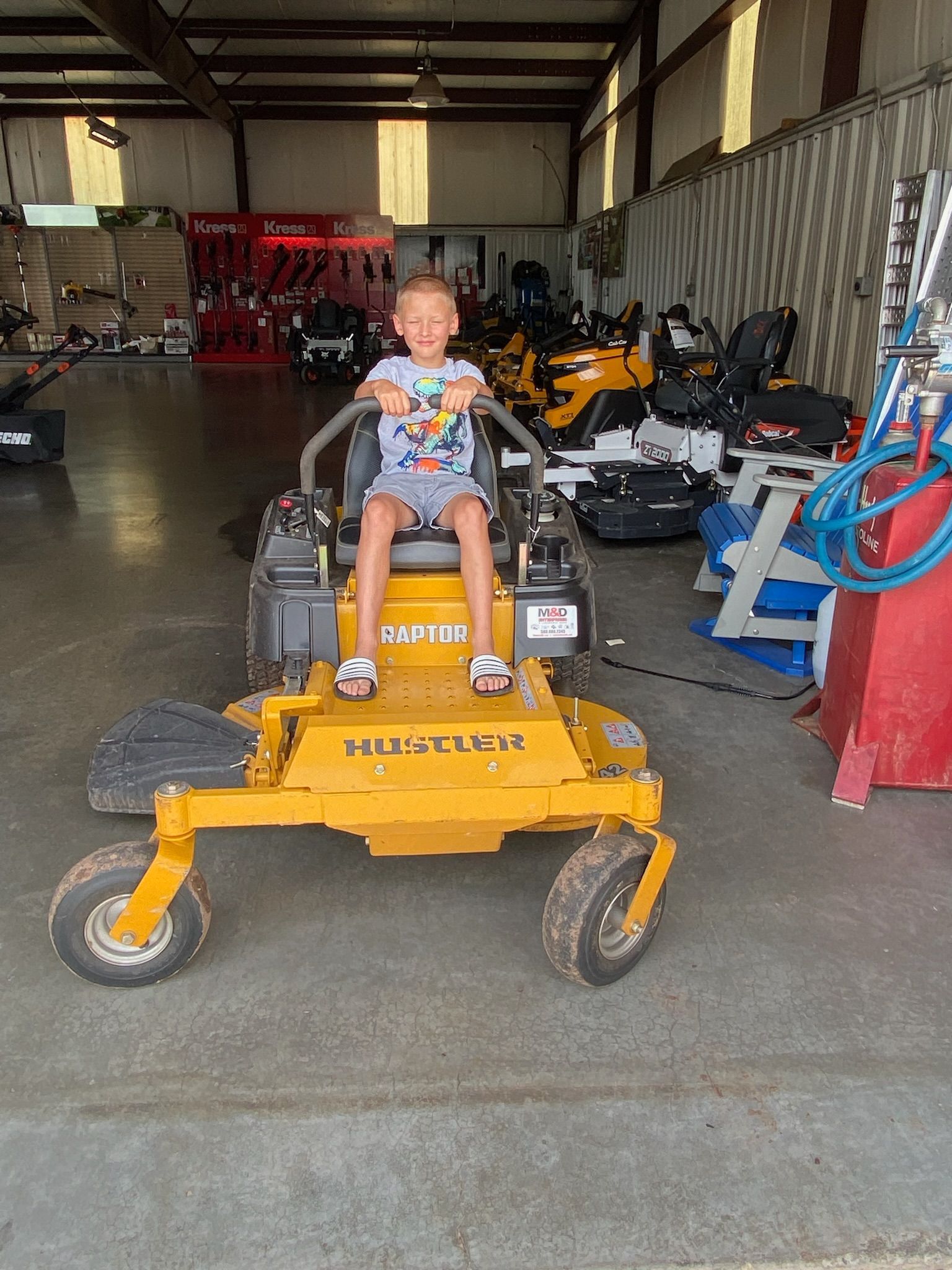 A little boy is sitting on a yellow lawn mower in a garage.