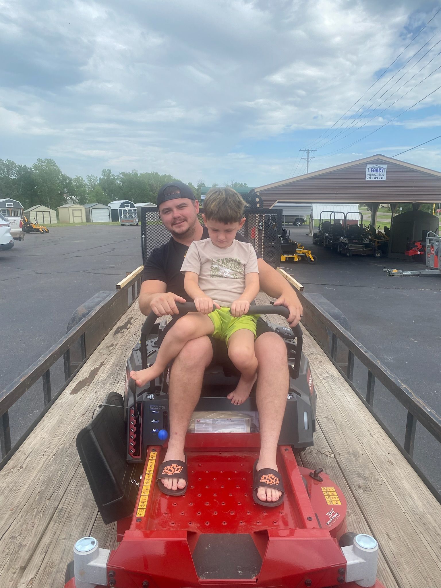A man and a little boy are riding a lawn mower on a trailer.