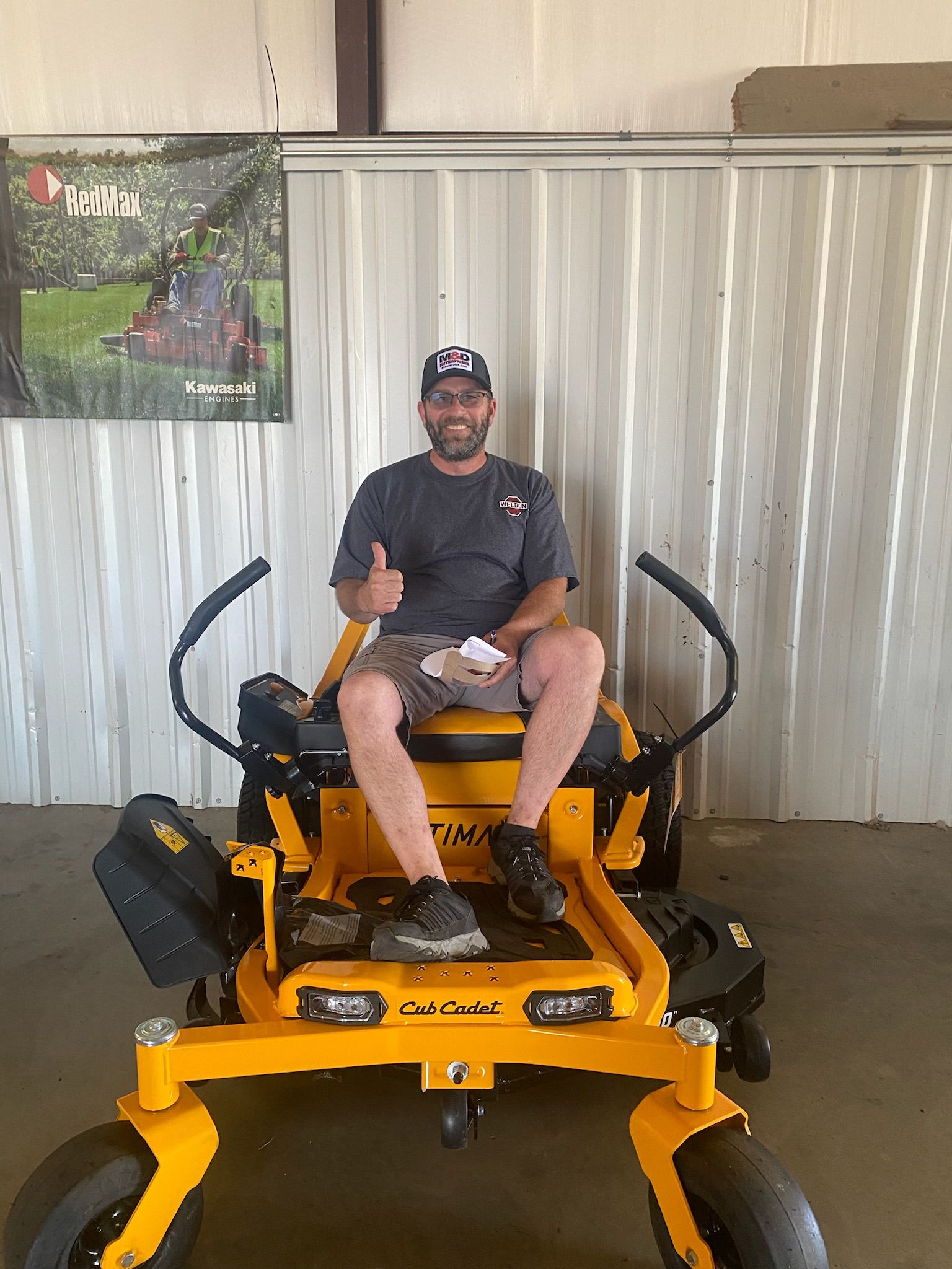 A man is sitting on a yellow lawn mower and giving a thumbs up.