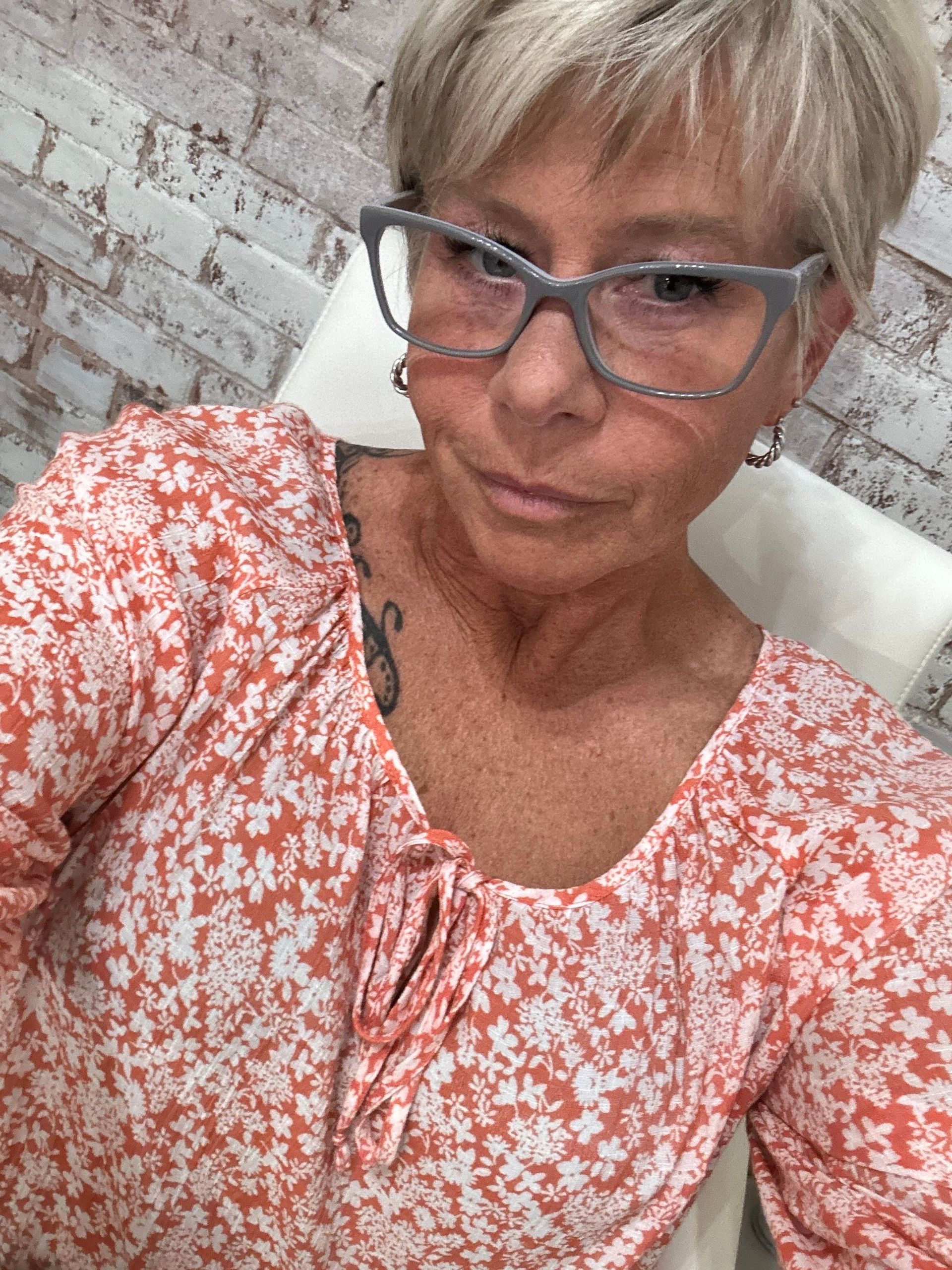 Una mujer con gafas y una camisa floral se está tomando una selfie.