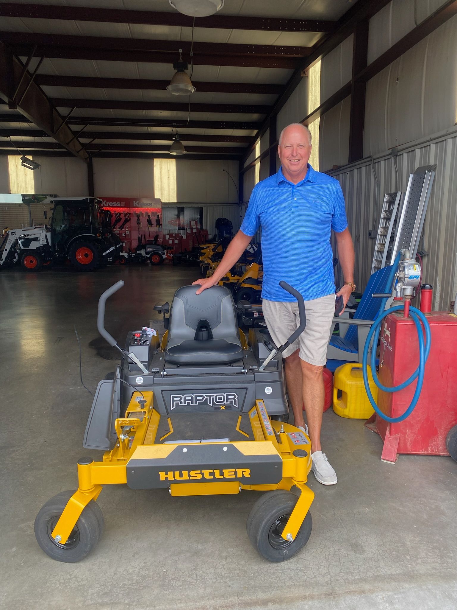 A man is standing next to a yellow and black lawn mower in a garage.