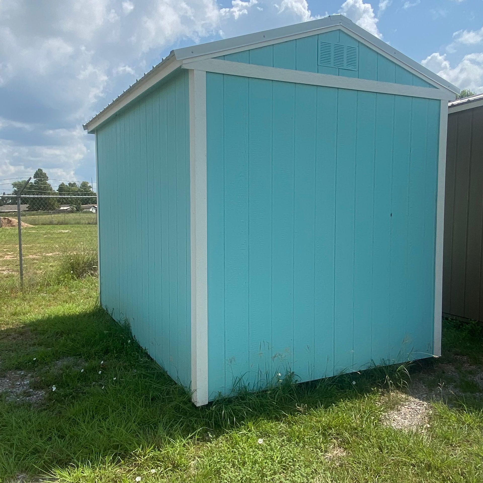 A blue and white shed is sitting in the middle of a grassy field.