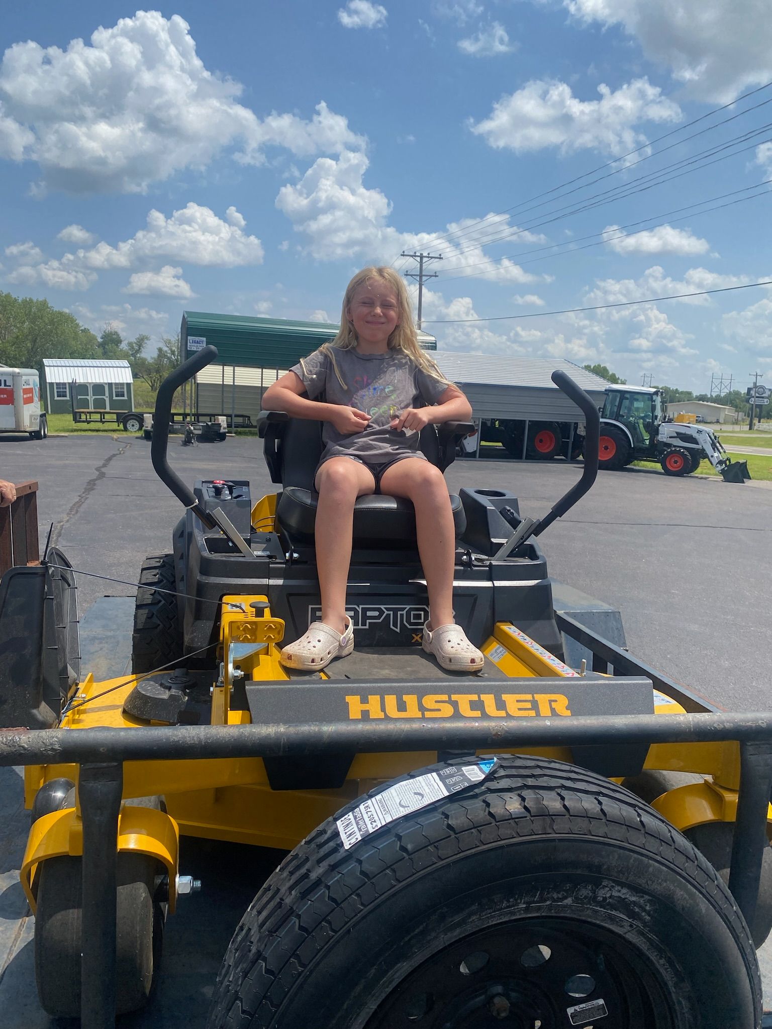 A little girl is sitting on a yellow lawn mower.