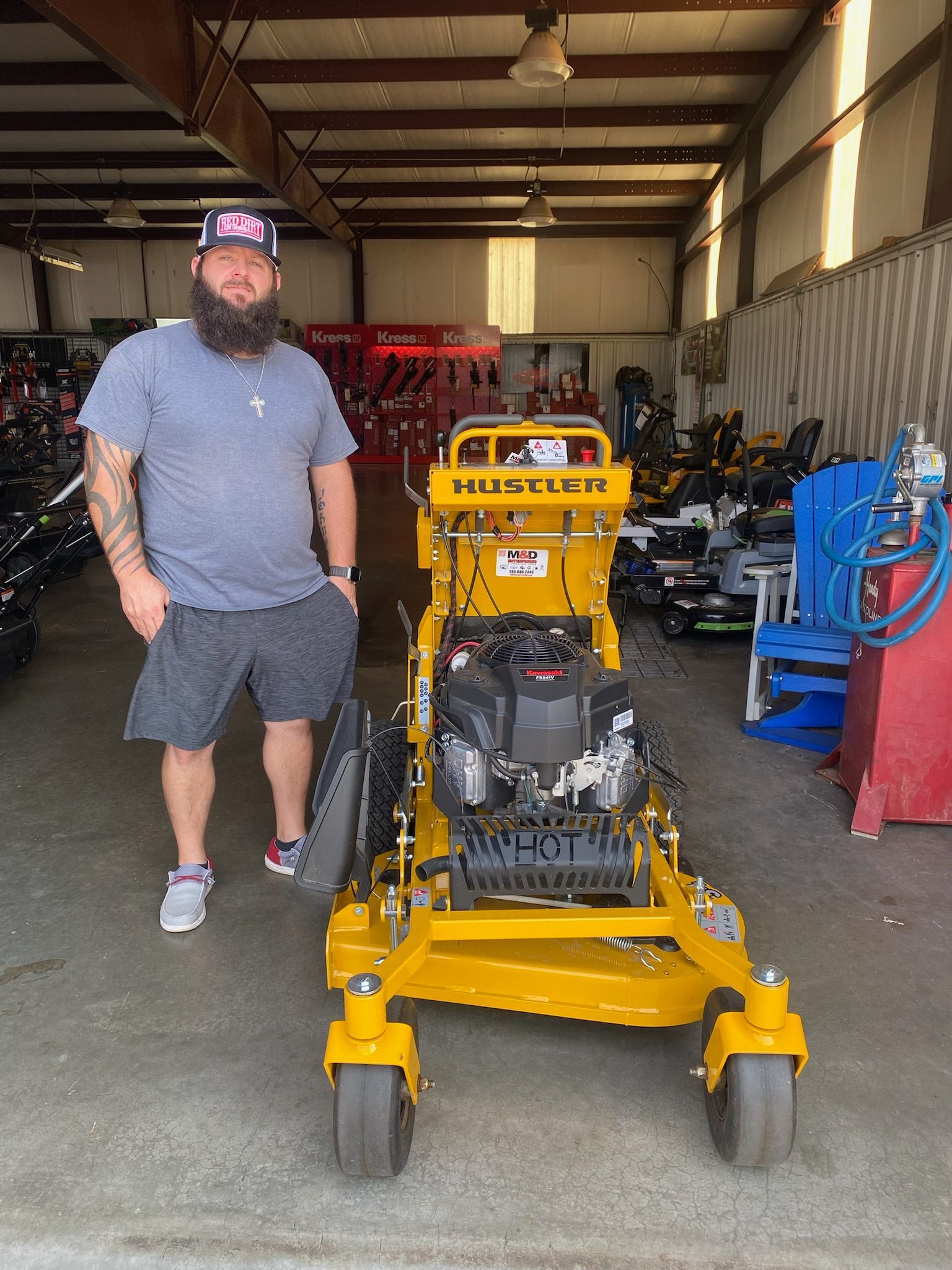 A man with a beard is standing next to a yellow lawn mower in a garage.