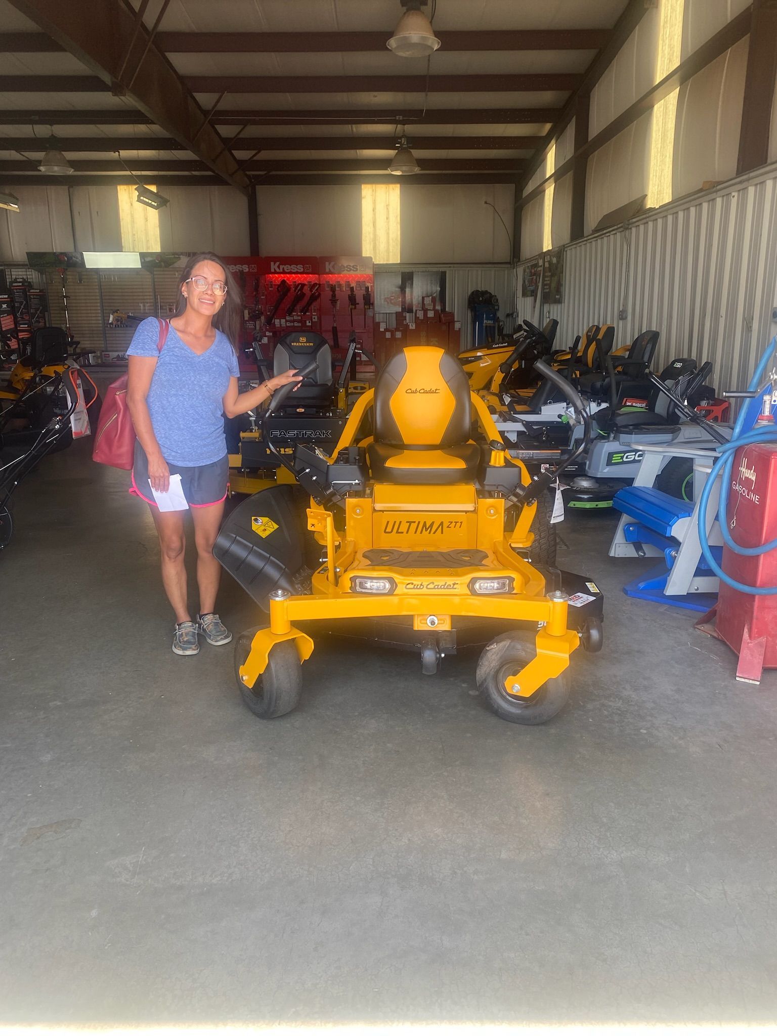 A woman is standing in front of a yellow lawn mower in a garage.