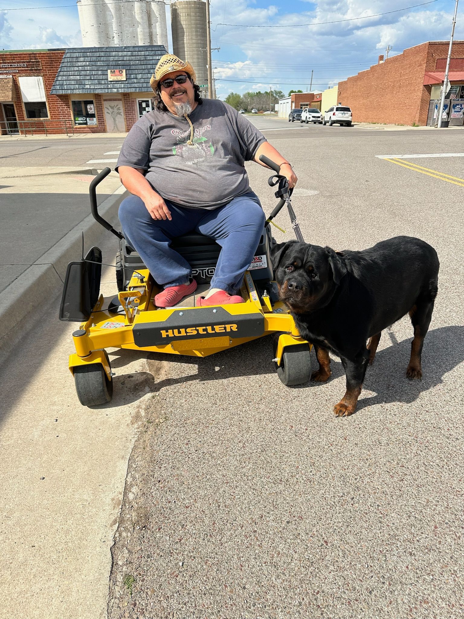 A man is sitting on a yellow lawn mower next to a black dog.