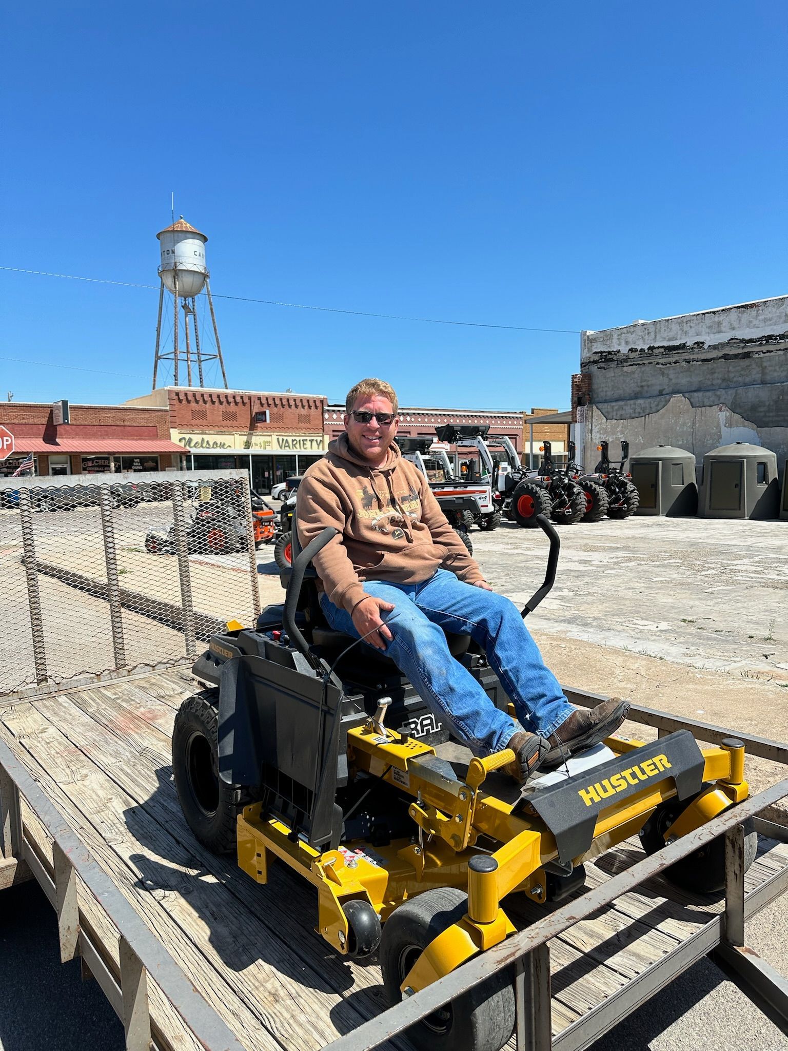 A man is sitting on a yellow lawn mower on a trailer.