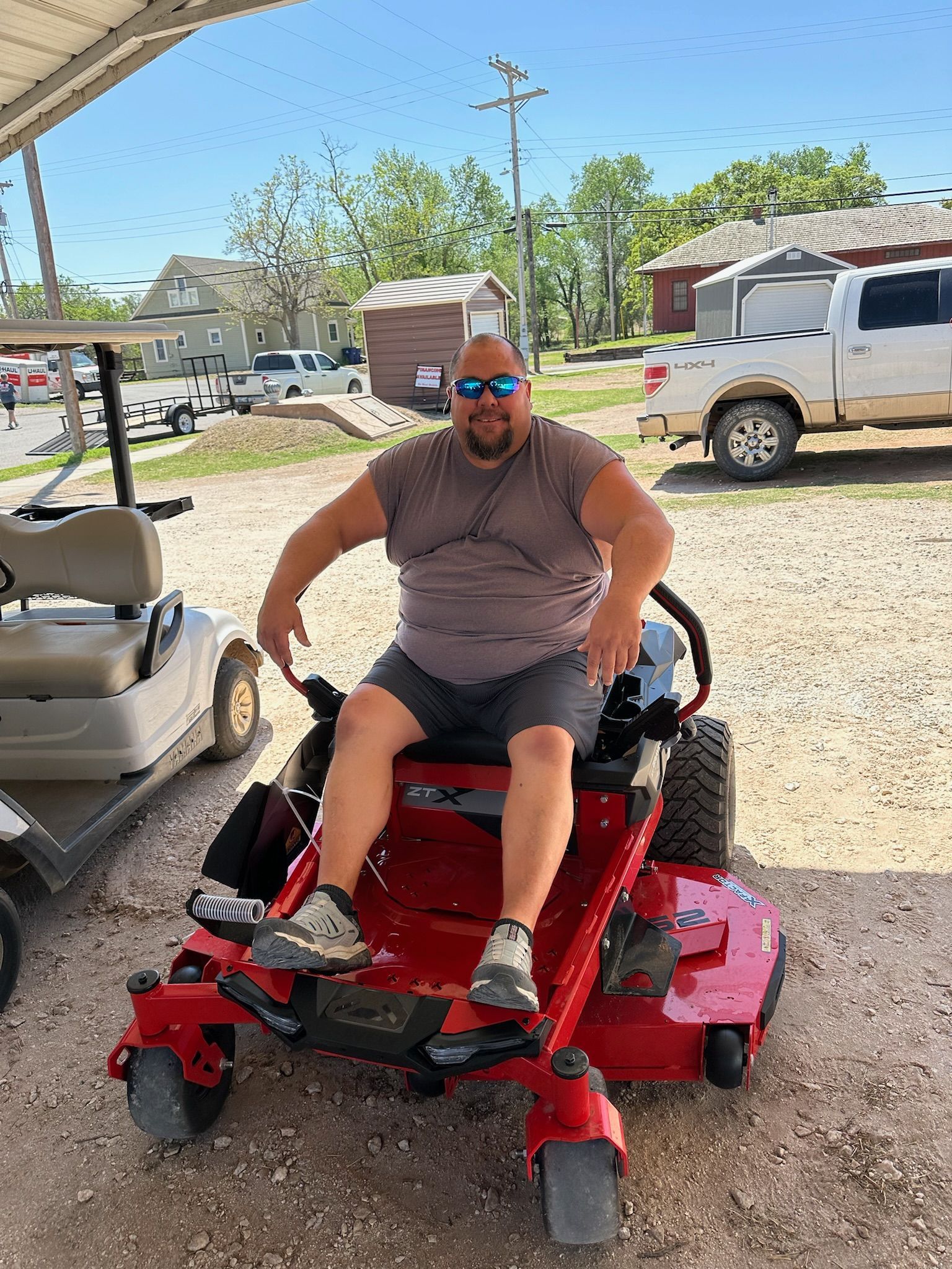 A man is sitting on a red lawn mower in a parking lot.