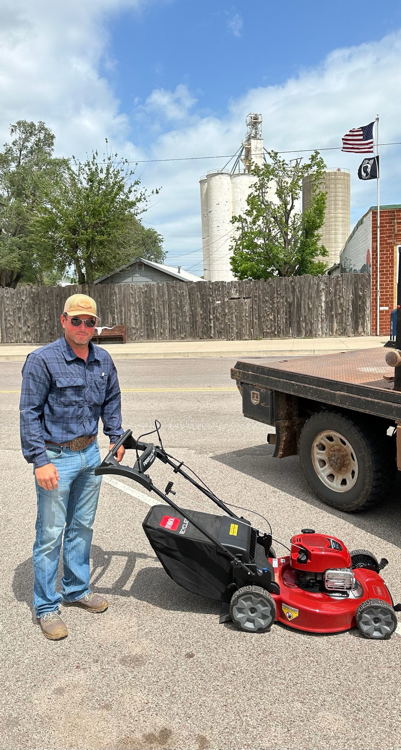 A man is standing next to a lawn mower in front of a truck.