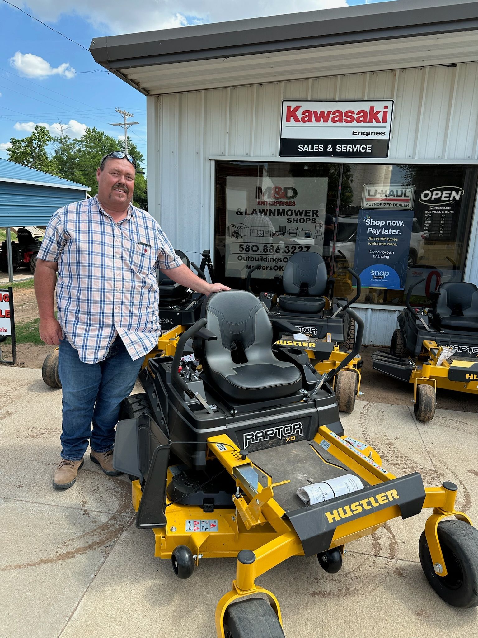 A man is standing next to a yellow lawn mower in front of a building.