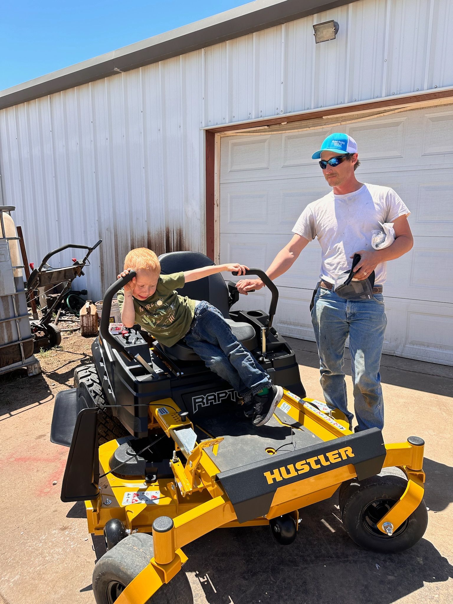 A man and a child are sitting on a yellow lawn mower.
