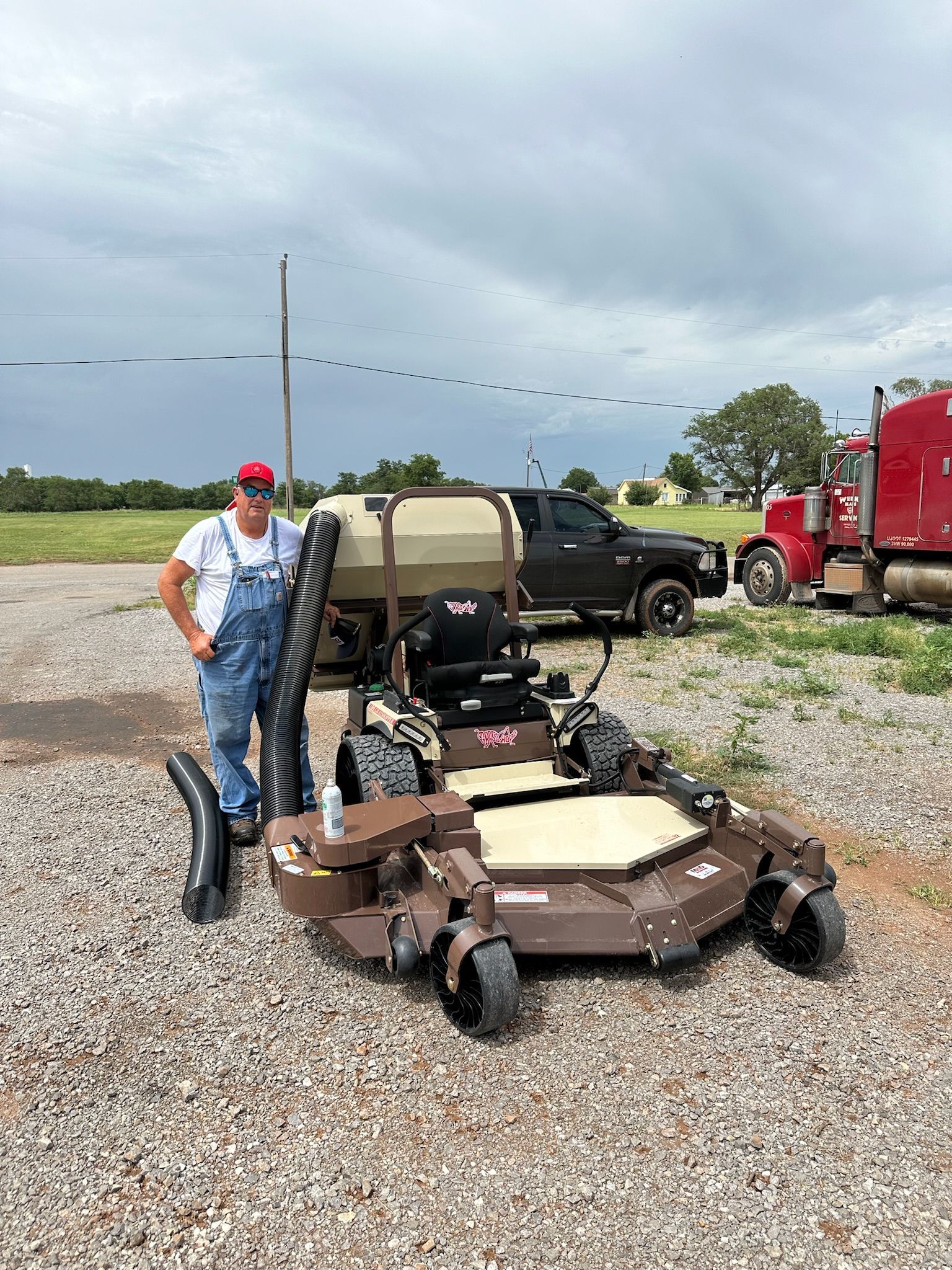 A man is standing next to a lawn mower in a gravel lot.