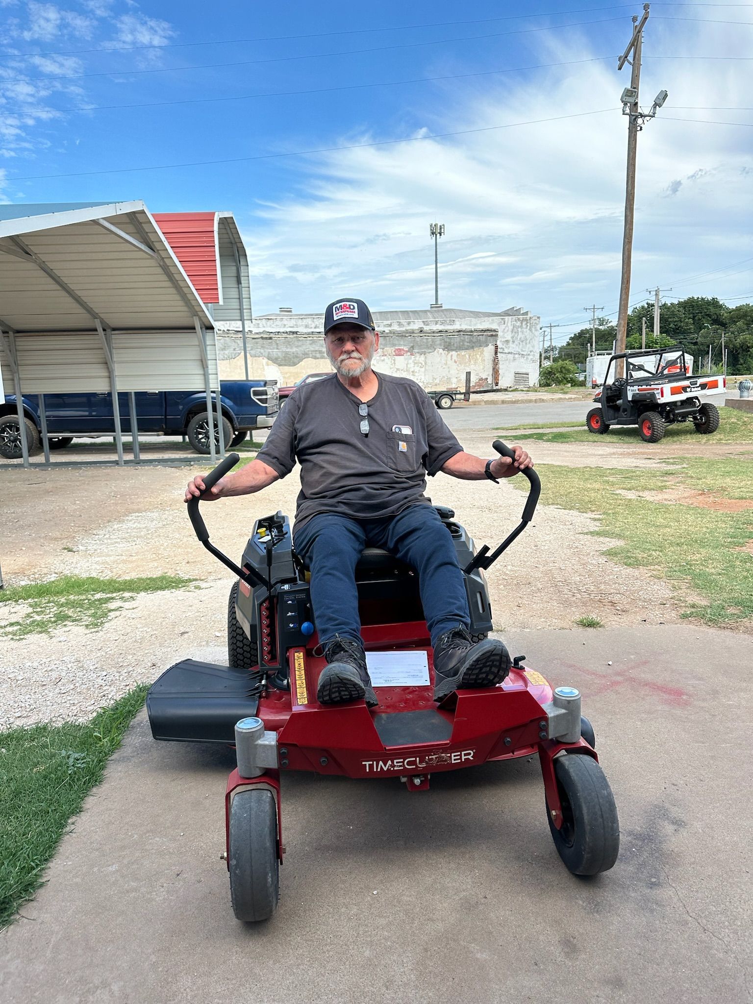 A man is sitting on a red lawn mower in a parking lot.