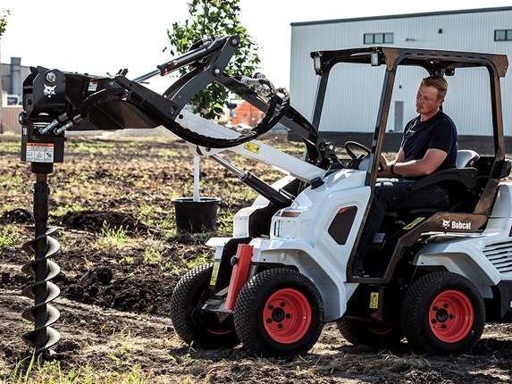 A man is driving a bobcat tractor in a field