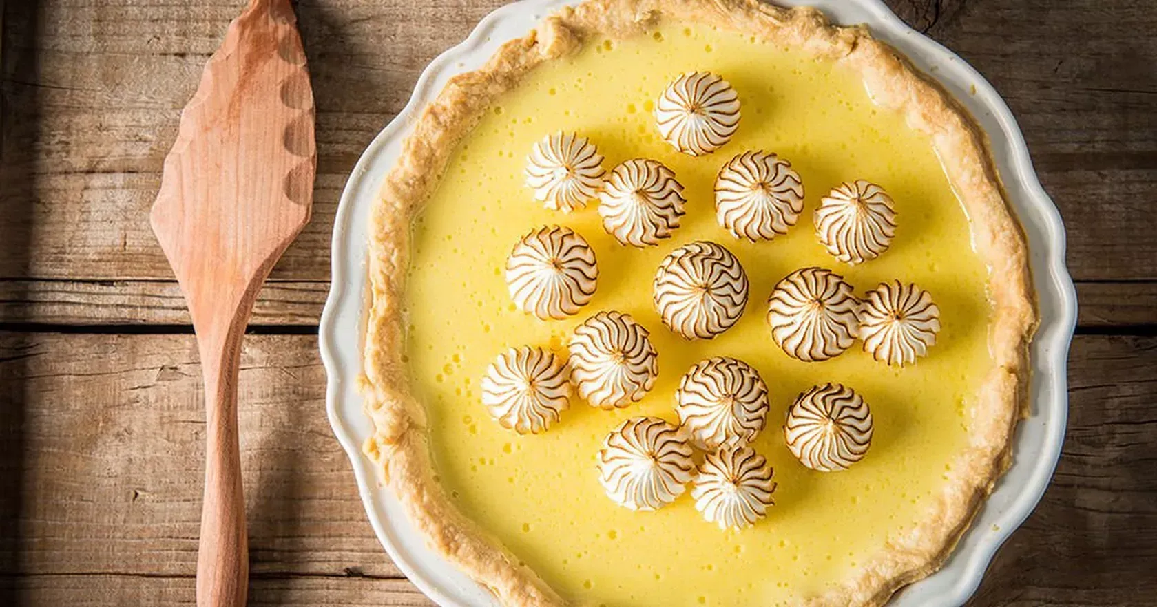 A lemon meringue pie is sitting on a white plate on a wooden table.