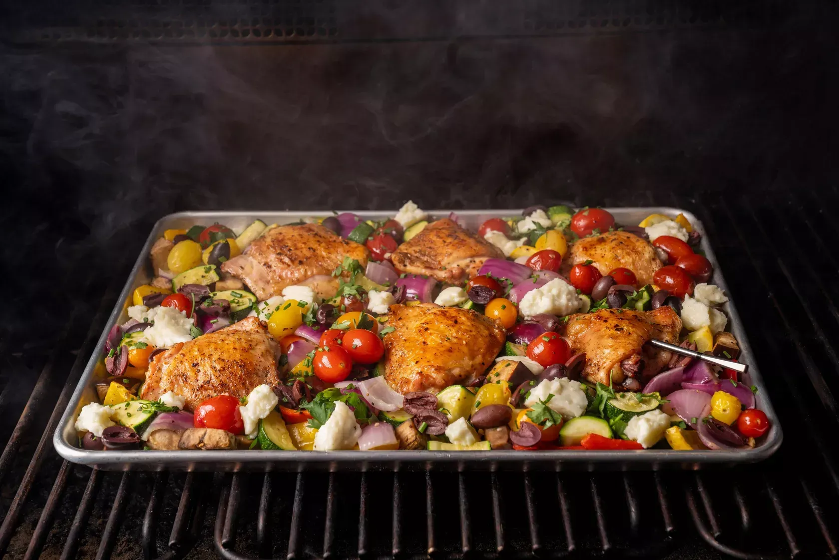 A pan of chicken and vegetables is cooking on a grill.