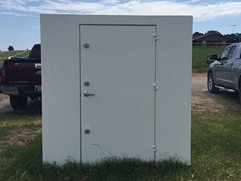 A a metal safe room s sitting in the grass next to a truck.